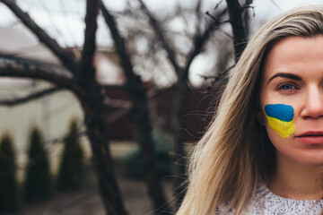 Outdoor portrait of young girl with blue and yellow ukrainian flag on her cheek