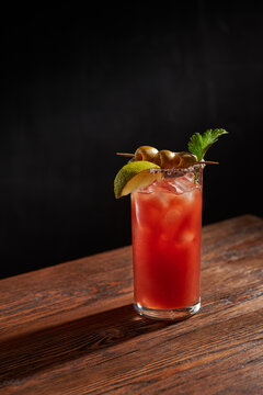 Iced bloody Mary (Caesar) cocktail with olives, parsley and lime piece in a glass, on a wooden bar and dark background. Vertical photo with shallow depth of field and copyspace.