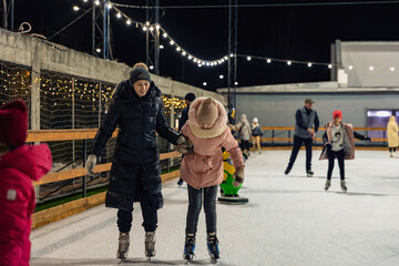 mother and daughter skate on the ice rink in the evening