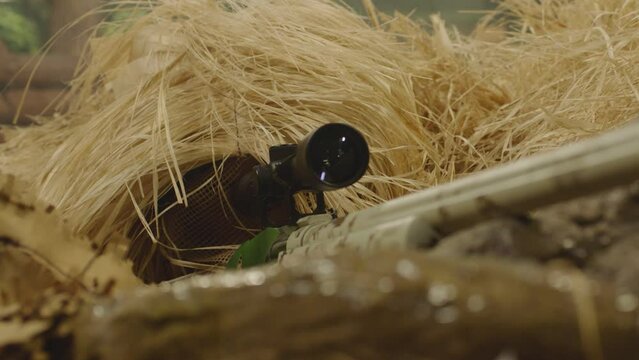 Close up view of sniper dressed in ghillie suit or grass cloak waiting and looking by rifle optics . Sharpshooter aims and shoots . Sharp shooter shooting . Shot on ARRI movie camera in Slow Motion 