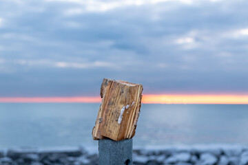A piece of stove sized  firewood (split) sits on an upright pole like a piece of sculture on a plinth with the dawn sky behind it.  Shot in the Toronto's Beaches neighbourhood. Room for text.