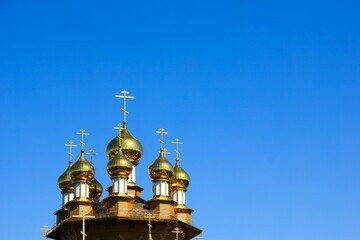 Fototapeta na wymiar Golden domes of wooden church on bright blue sky background