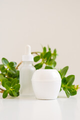 Obraz na płótnie Canvas White jar of cream and a bottle with dropper from serum on a white neutral natural light. Still life minimalistic beauty cosmetic template for beauty business and industry. Bright fresh green leaves.