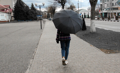 A girl under an umbrella walks down the street