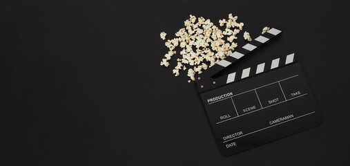 Black clapper board or movie slate and popcorn on black background.