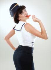 Naughty in naughtical. A sailor pinup girl posing against white with a lollipop.