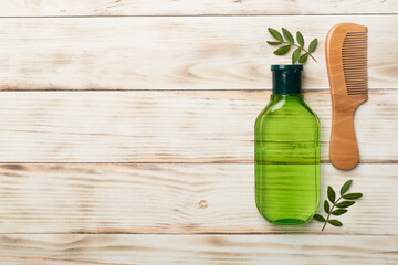 Shampoo with herbal extract and comb on wooden background, top view