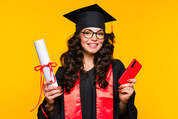 Girl graduate in graduation hat and eyewear with diploma and smartphone on yellow background....