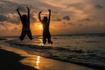 Silhouette of two young girls jumping and having fun at the beach