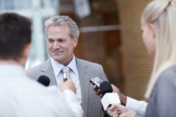 Do you have a comment sir. Shot of a mature businessman being interviewed by reporters.