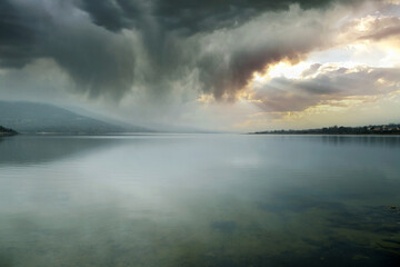 stormy landscape on mountain lake with clouds breaking open by the sun - Powered by Adobe