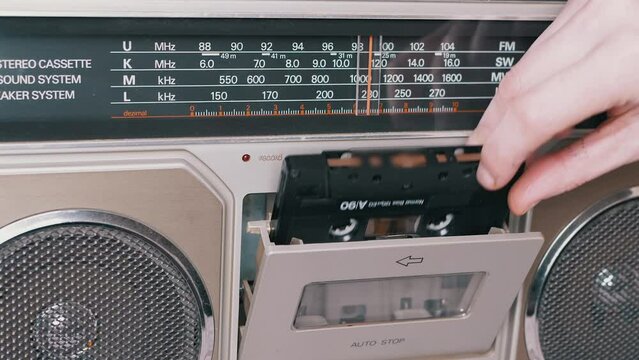 Female Hands Take Out, Turn Over an Old Audio Cassette from a Tape Recorder. Classic black retro 90s magnetic tape cassette for listening to music. Disco 80s, 90s disco style. Portable stereo player.