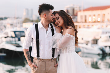 Happy lovers, the bride and groom in elegant wedding dresses go on a honeymoon by sea on  yacht in the marina in Sochi in summer outdoor. Off-site chamber wedding ceremony for a married couple in love