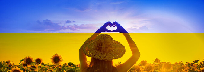 Stop war concept. Girl in a hat shows a heart on a background of the peaceful sky and sunflower...