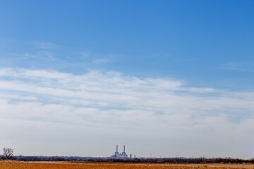 Fototapeta premium A Harvested Field and a Coal Electric Plant Against a Big Blue Sky