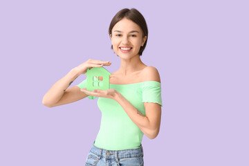Beautiful young woman with figure of house on color background