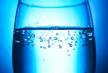 Glass of clear water on blue background, closeup