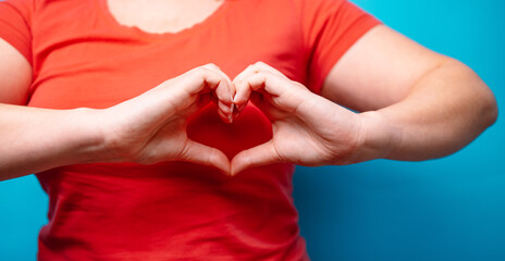 Woman in red T-shirt with hands making heart shape on blue background. People affection and care concept