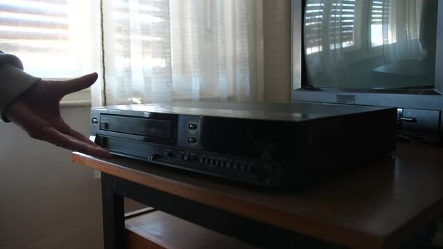 woman pressing eject button on video cassette recorder, tape coming out, wide static