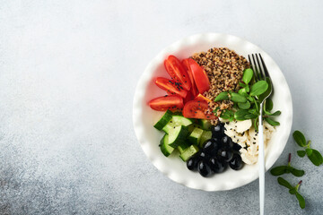 Buddha bowl dish with tomato, cucumber, mozzarella cheese, quinoa, olives and microgreens. Detox and healthy keto diet bowl concept. Healthy and balanced food concept. Top view, flat lay, copy space