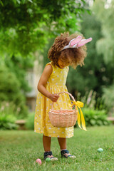 Little Black girl with bunny ears gathering Easter eggs