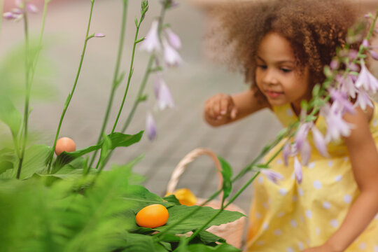 Little Black girl wearing bunny ears gathering Easter eggs
