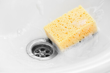 Yellow cleaning sponge with foam in ceramic sink, closeup