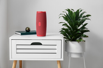 Wireless portable speaker on bedside table and houseplant near light wall in room