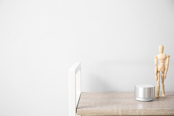 Wireless portable speaker and wooden mannequin doll on table near light wall