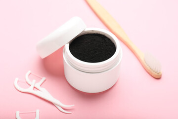 Jar with activated charcoal tooth powder, floss toothpicks and toothbrush on pink background
