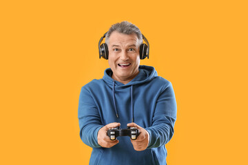 Happy senior man in headphones with game pad on yellow background © Pixel-Shot