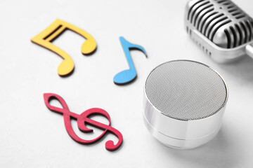Wireless portable speaker, microphone and music notes on light background, closeup