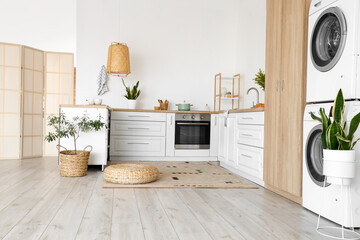 Interior of light kitchen with washing machines, white counters and cupboard