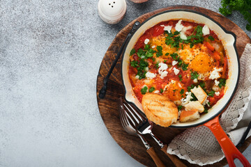 Shakshuka Homemade fried eggs poached in sauce of tomatoes, olive oil, peppers, onion and garlic in iron frying pan on old grey slate background. Traditional cuisine of Israel. Late breakfast concept