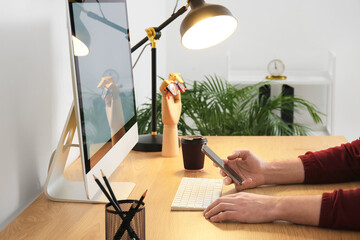 Man working with modern computer and checking mobile phone on wooden table