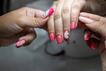 Obraz na płótnie Canvas Manicurist performing the process of applying red acrylic nails with flower decorations, in a beauty salon