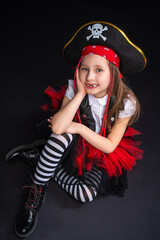 Portrait of a naughty little girl in a pirate costume, sitting on a black background, A girl is preparing for the Halloween holiday.