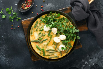 Frittata. Omelet with spinach and green beans, healthy food in black frying pan on dark old rustic background. Healthy breakfast delicious. Top view flat lay. Copy space.