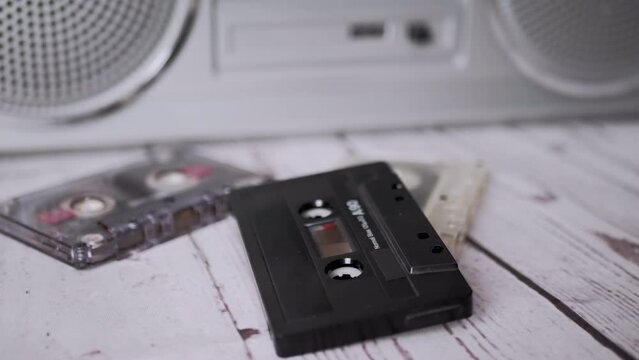 Female Hands Throwing an Old Black Audio Cassette on Table. Trash. A stack of vintage, obsolete, music magnetic tape cassettes from the late 80s, 90s lie on a table near a tape recorder. Nostalgia.