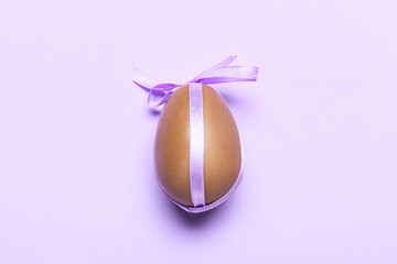 Delicious chocolate egg with ribbon on purple background
