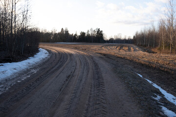winding sand and gravel dirt road in Latvia countryside, melting snow on roadsides