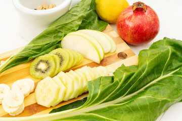 A kitchen cutting board with kiwifruit apples and cucumbers on top