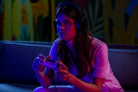 Female gamer playing video game sitting on couch in dark room.