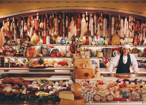 Associate in Chefs hat at deli counter with large selection of imported meats and cheeses 