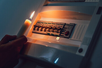 Energy crisis. Hand in complete darkness holding a candle to investigate a home fuse box during a...