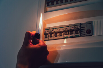 Energy crisis. Hand in complete darkness holding a lighter to investigate a home fuse box during a...