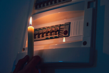 Energy crisis. Hand in complete darkness holding a candle to investigate a home fuse box during a...