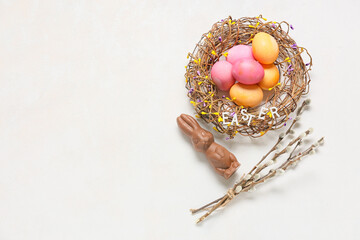 Obraz na płótnie Canvas Nest with colorful Easter eggs, chocolate bunny and pussy willow branches on light background