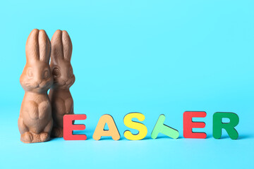 Word EASTER and chocolate bunnies on color background