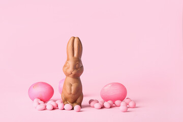 Easter chocolate bunny, candies and eggs on pink background